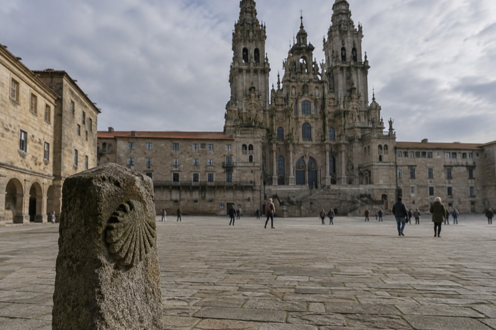 A stone pilgrim marker with a yellow arrow and scallop shell pointing the way along the Portuguese Camino