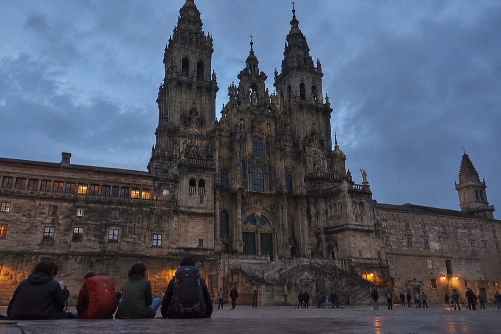 Pilgrims with backpacks resting on the stone pavement beside the Cathedral in Santiago de Compostela