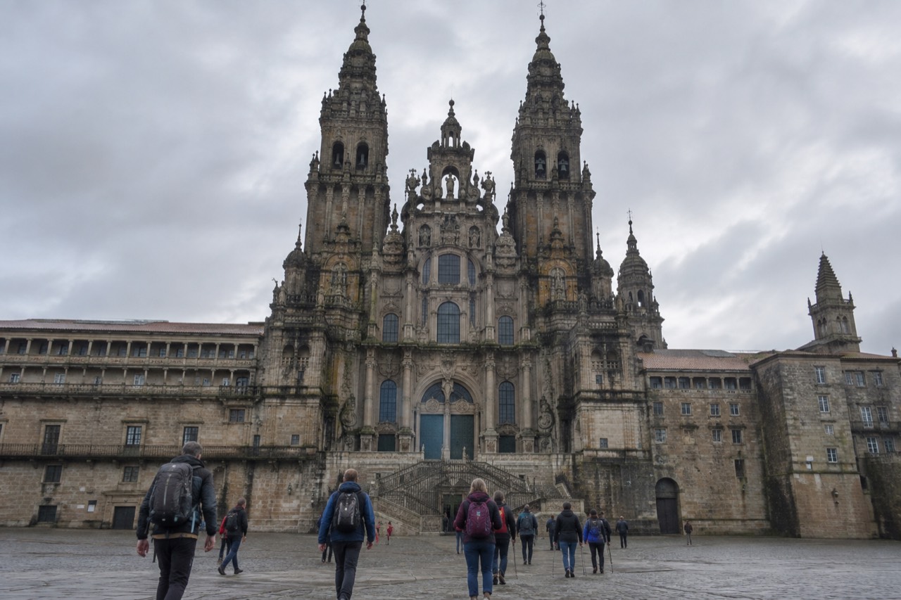 Pilgrims with backpacks walking into Praza do Obradoiro beside the Cathedral of Santiago de Compostela