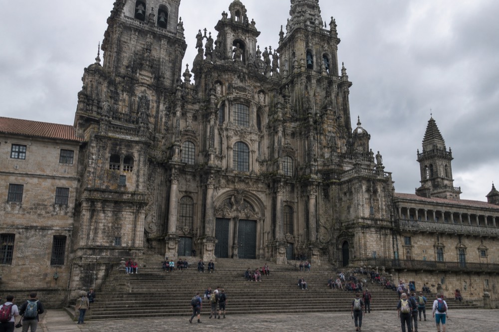 Pilgrims resting with backpacks on the stone steps in front of the Cathedral facade in Santiago de Compostela