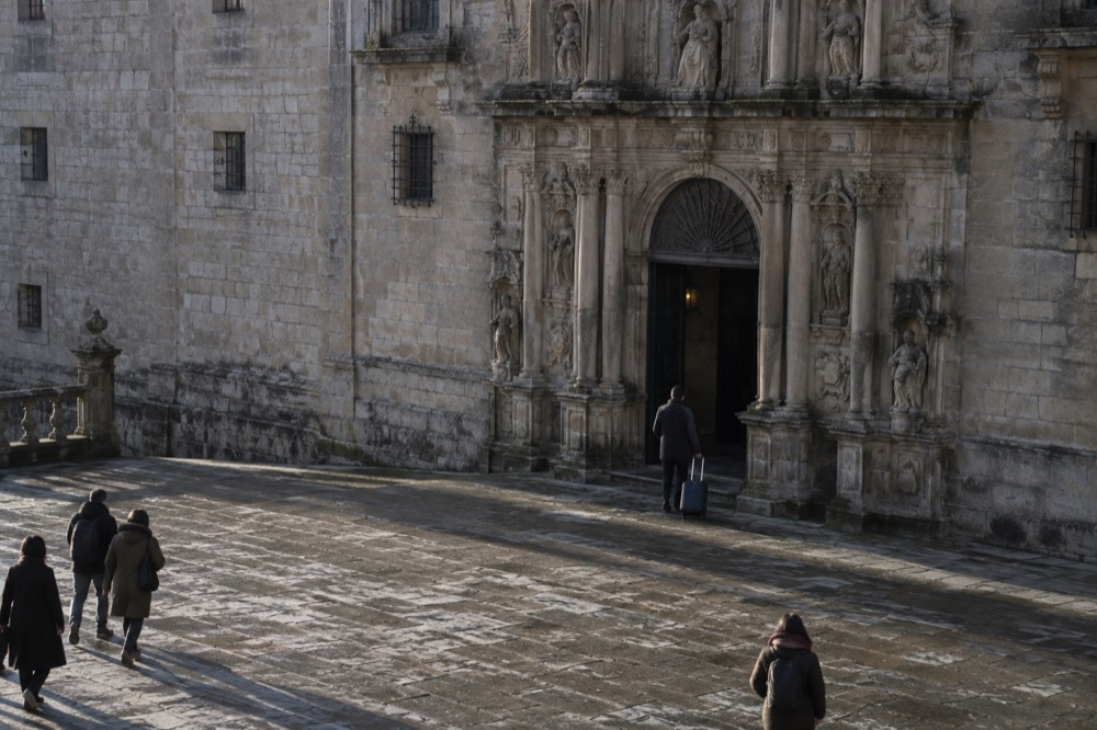 A guest arriving with luggage at the arched entrance of the Parador Hostal dos Reis Catolicos in Santiago de Compostela