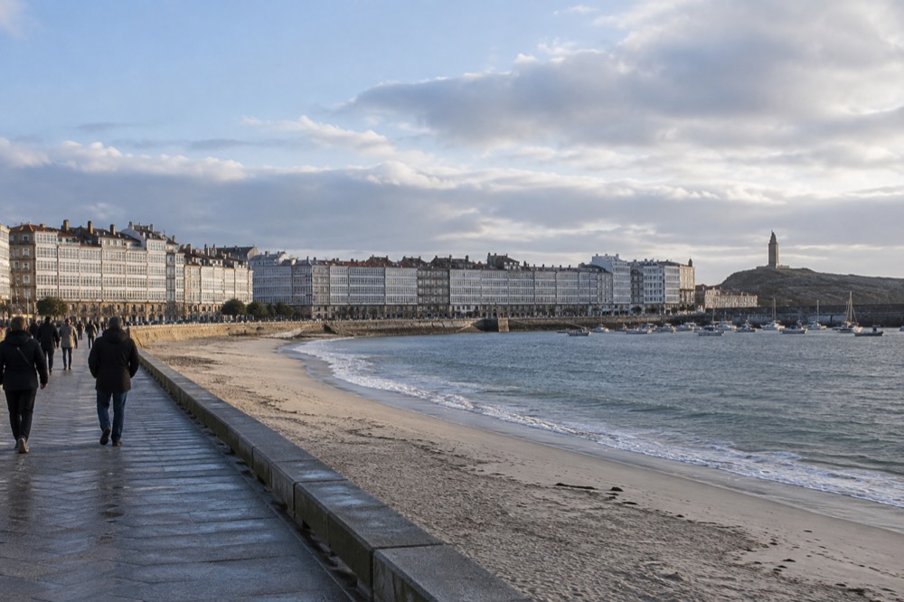 People strolling along a wide seafront promenade beside a sandy urban beach