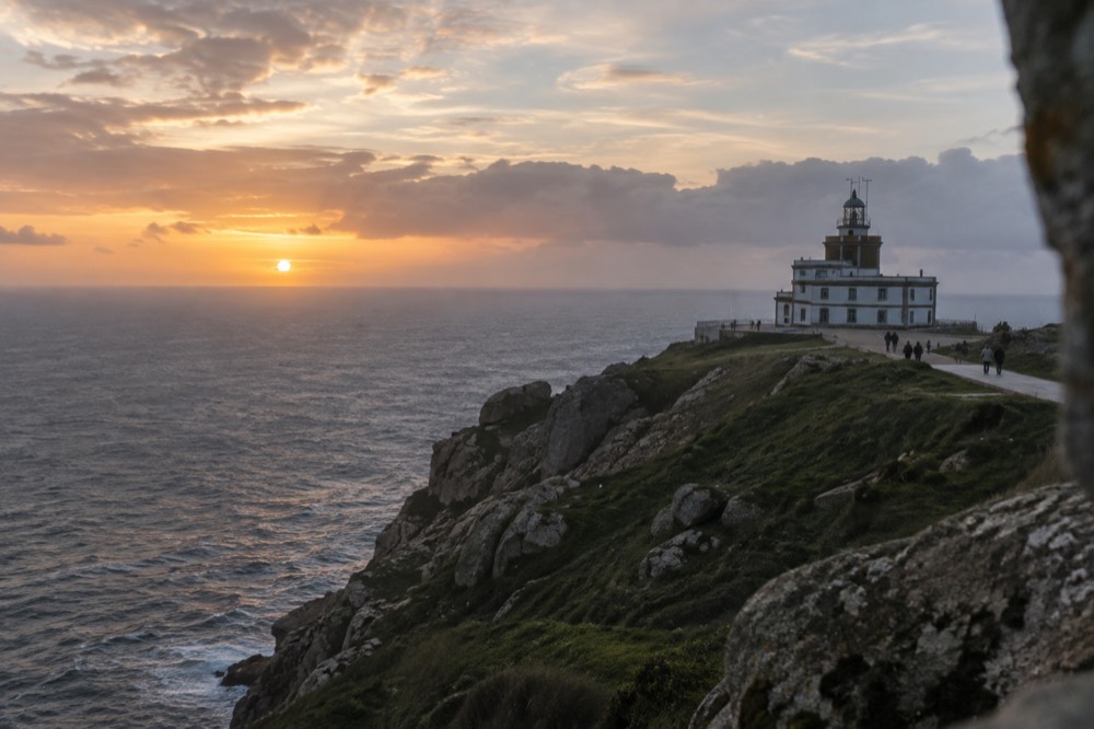 The lighthouse at Fisterra headland overlooking the Atlantic at sunset with a few walkers on the path