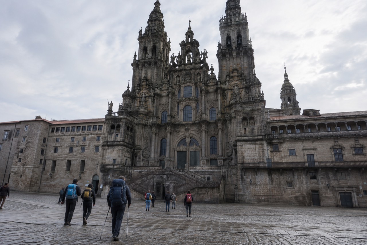 Pilgrims in hiking clothes walking quietly through the stone nave of Santiago de Compostela Cathedral