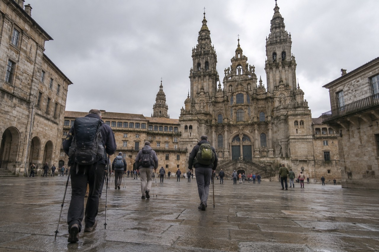 Pilgrims with backpacks and walking sticks arriving on a stone street toward the cathedral towers of Santiago de Compostela