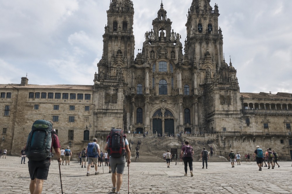Pilgrims arriving on foot into the stone square in front of Santiago de Compostela Cathedral with backpacks and walking sticks