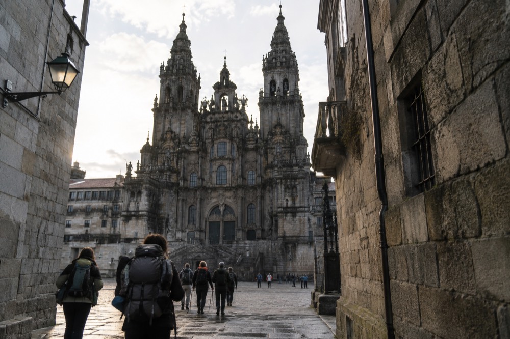 Arriving pilgrims with backpacks walking through a narrow granite-walled street in Santiago de Compostela