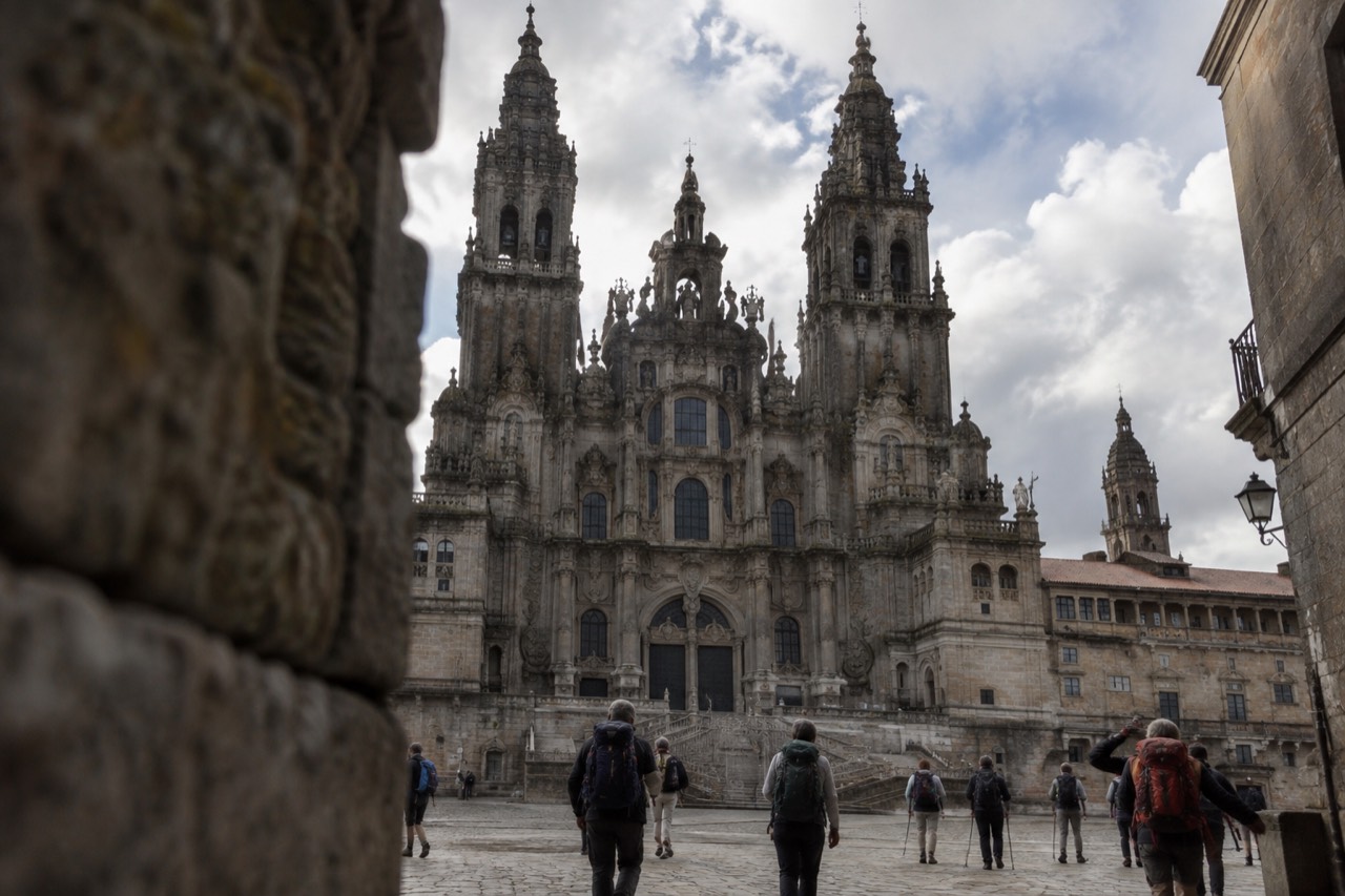 Pilgrims walking a green Galician path toward the towers of Santiago de Compostela Cathedral