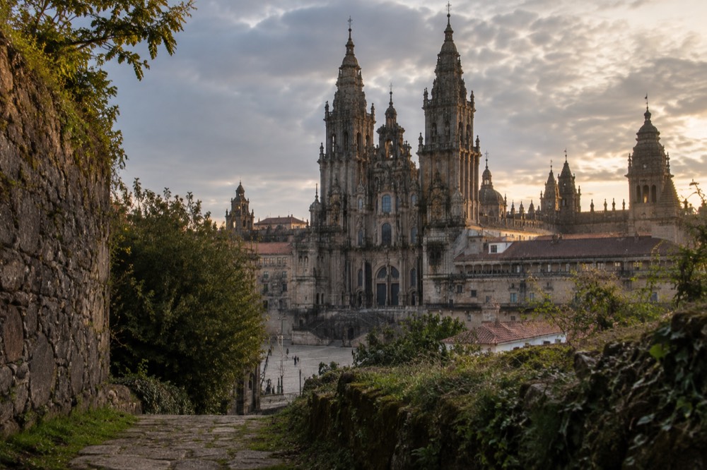 The stone facade of Santiago de Compostela Cathedral seen from a green hillside path