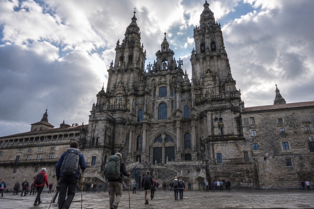 Pilgrims arriving in front of the Cathedral of Santiago de Compostela with backpacks and walking staffs