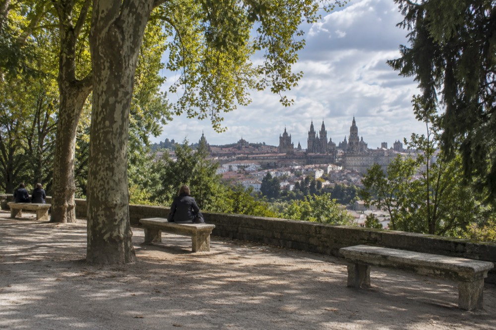 Benches along a tree-lined walk in Alameda Park with the old town rooftops beyond