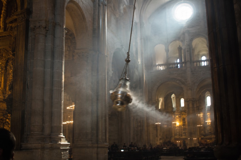 Incense smoke drifting through sunlit stone arches inside a cathedral transept
