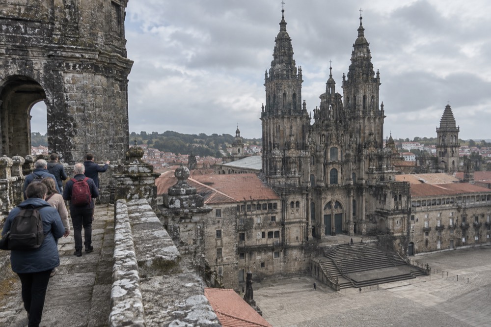 A guide leading a small group along a stone rooftop walkway beside a cathedral tower