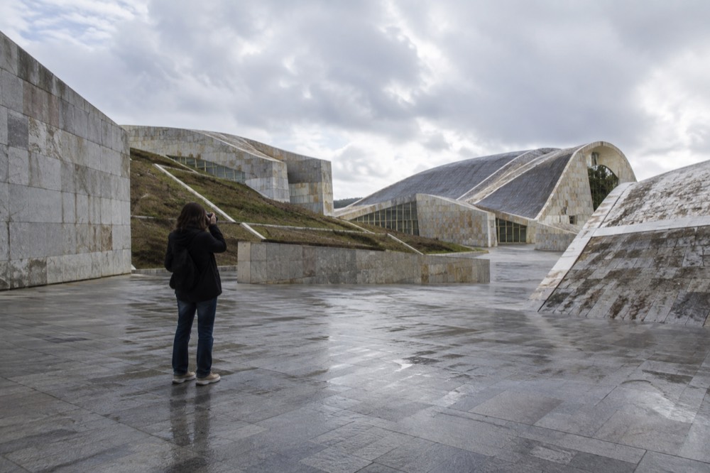 A quiet stone plaza inside a modern cultural complex with a single visitor taking a photograph