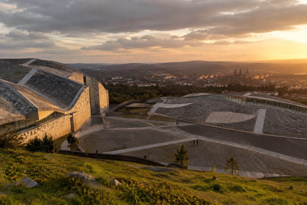 Sunset light on pale modern stone walls with the historic city glowing in the valley below