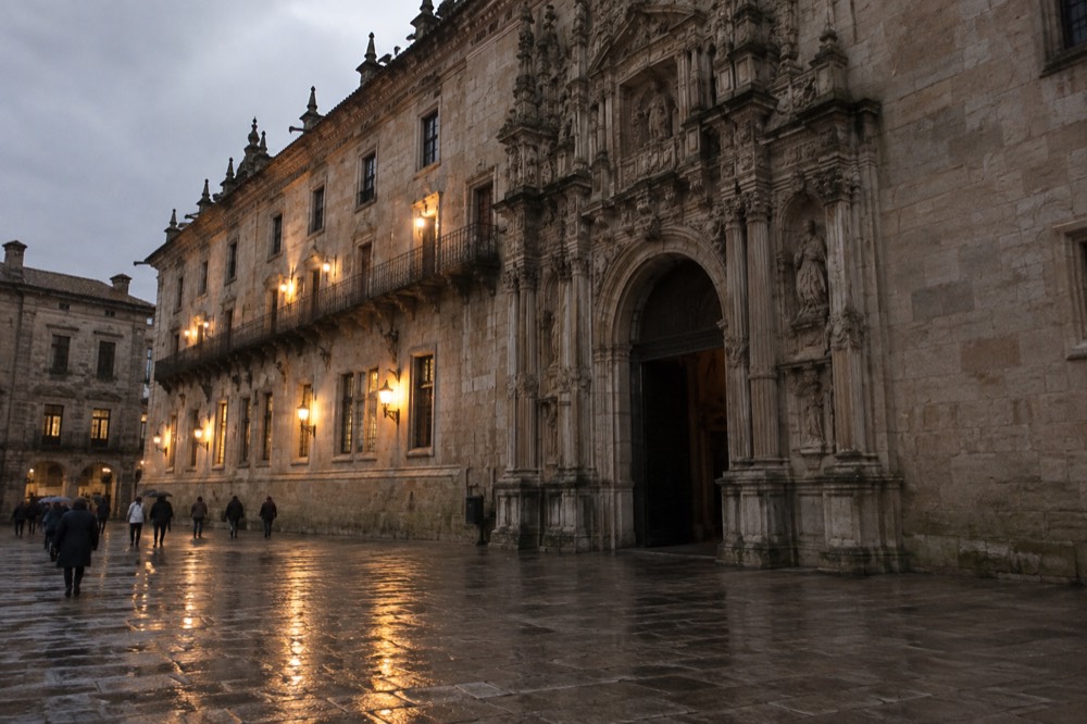 Rain-wet granite pavement reflecting the lights of the Parador facade at dusk