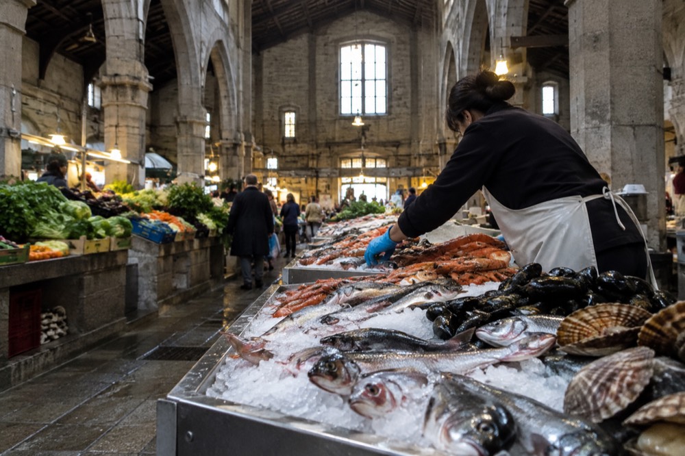 A fishmonger arranging shellfish and whole fish on crushed ice at a market counter