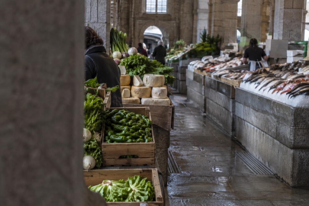 Crates of green Padrón peppers and Galician cheeses stacked at a produce stall