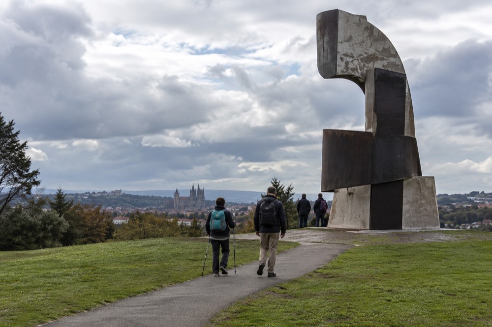 A large concrete pilgrim monument sculpture standing on the hilltop with walkers nearby