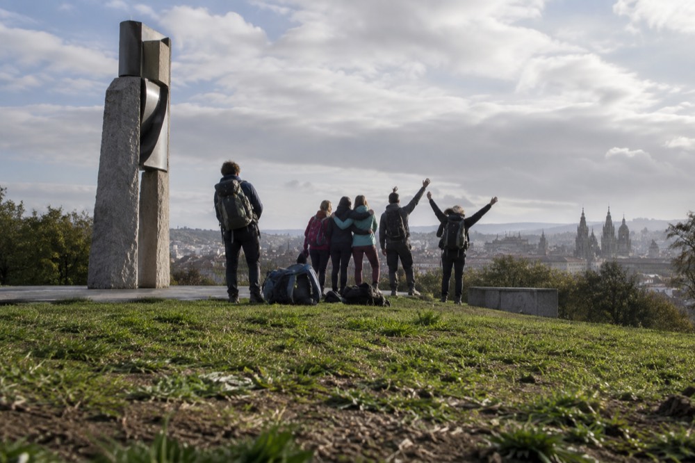 Pilgrims with backpacks celebrating together at the viewpoint as the Cathedral appears on the horizon