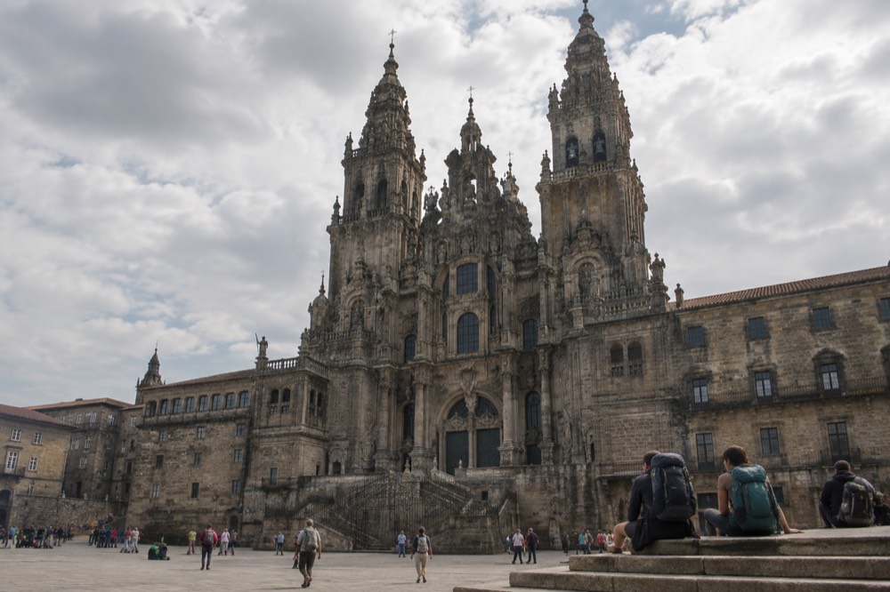 Pilgrims with backpacks resting on stone steps near a historic building in Santiago de Compostela