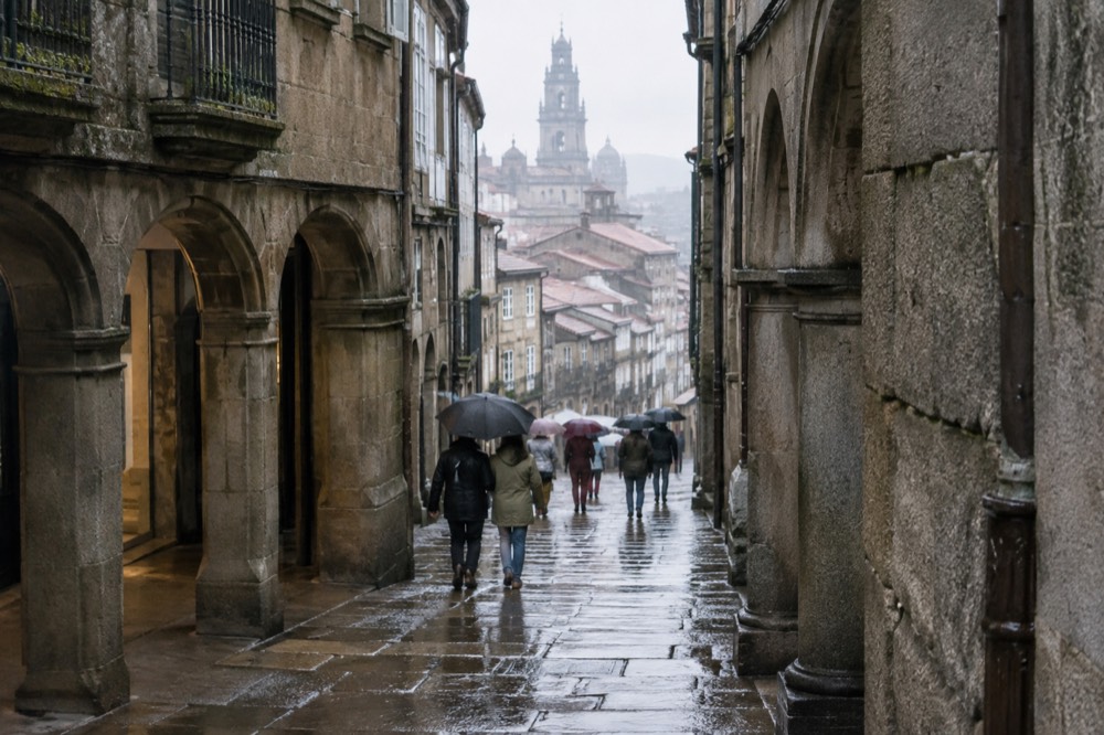Wet granite street in the old town of Santiago de Compostela with reflections and umbrellas