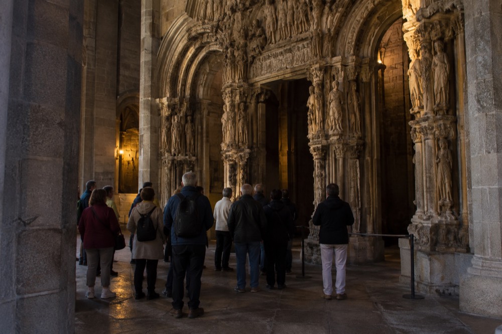 Visitors on a guided tour standing among the carved arches of the Portico da Gloria