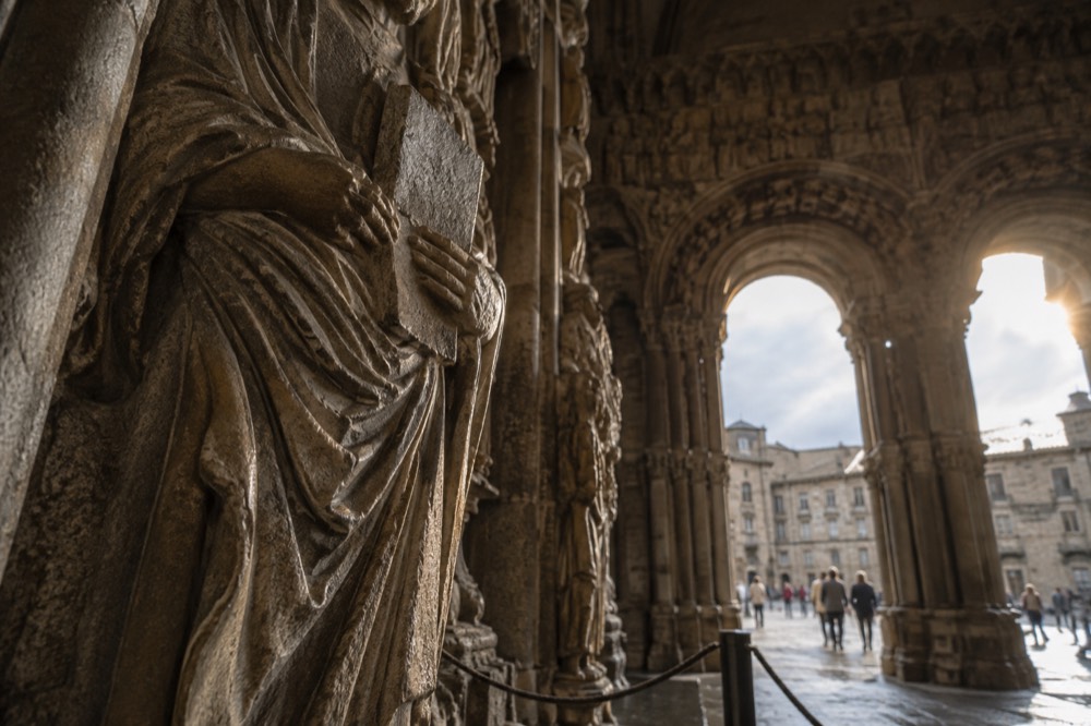 Detail of a carved apostle holding a book in the Portico da Gloria with deep folds of stone drapery
