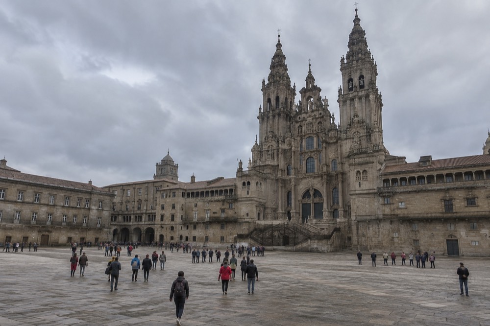 Pilgrims and visitors crossing the open flagstones of Praza do Obradoiro toward the Cathedral's twin west towers