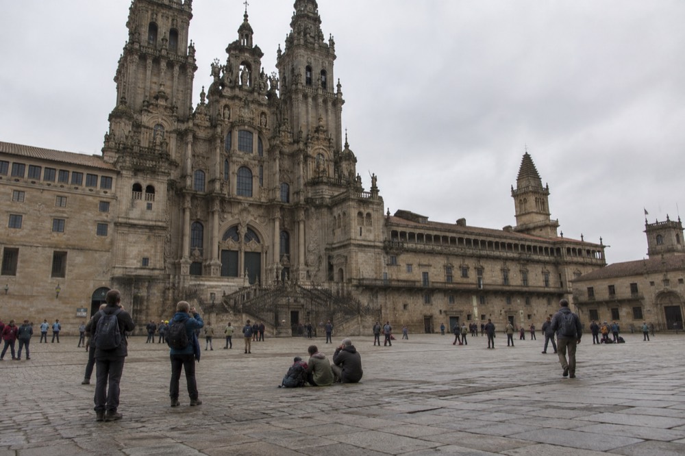 Tired pilgrims with backpacks resting and taking photographs on the square at the end of the Camino