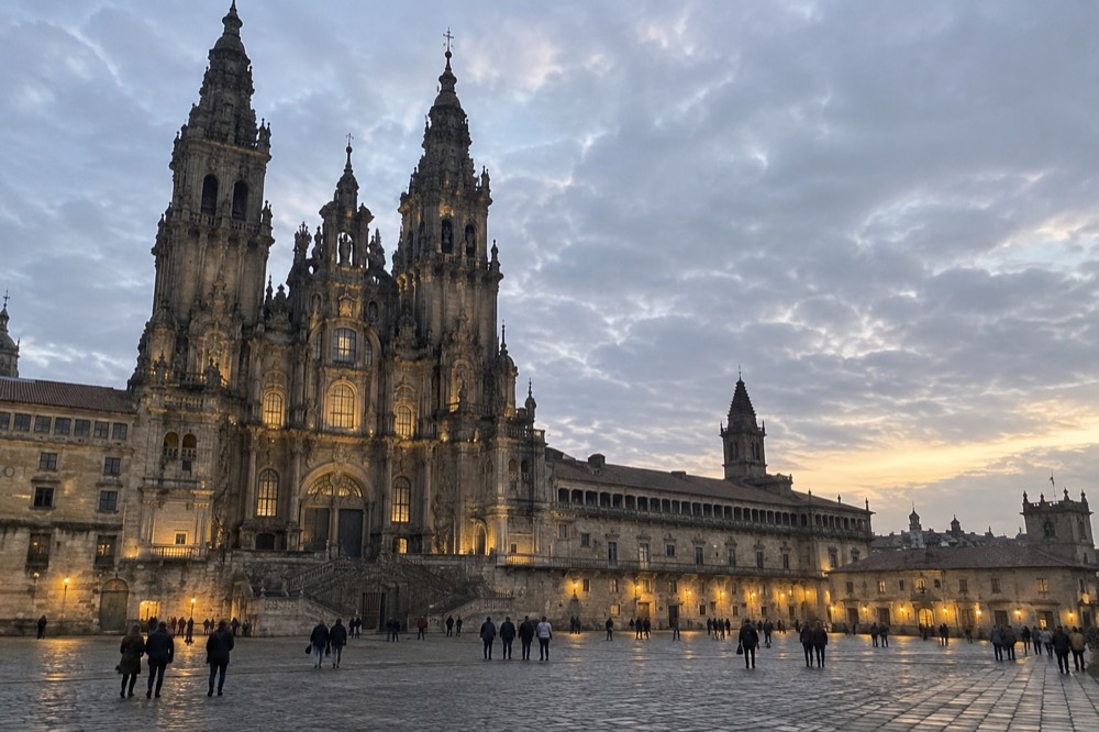 The full width of the square at dusk with the lit Cathedral facade and the Parador beyond
