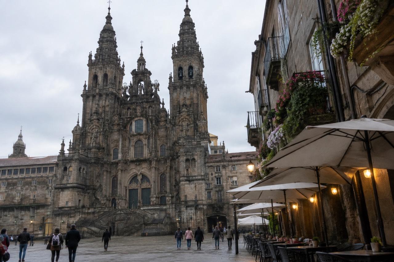 Evening view along a narrow granite street in Santiago de Compostela with restaurant awnings and lit terraces either side