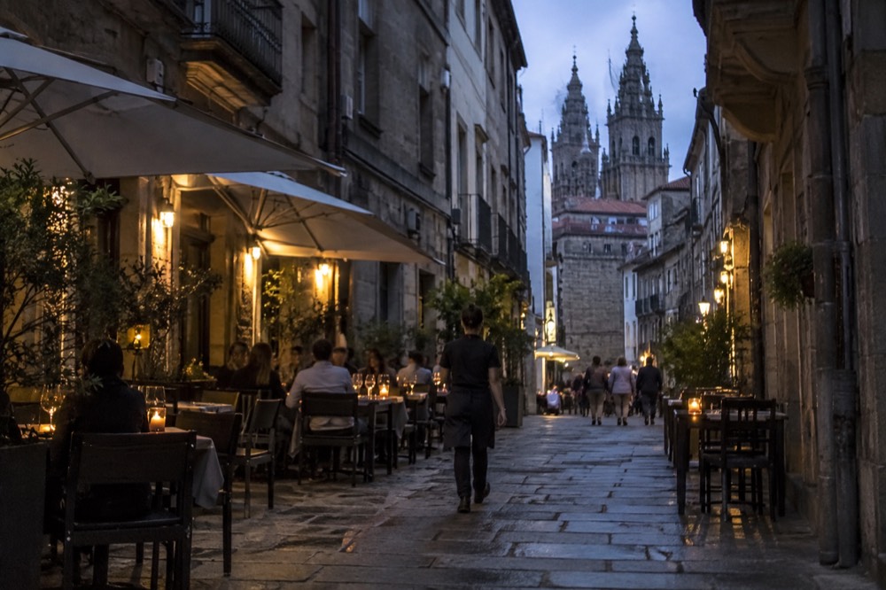 A terraced restaurant on a narrow street with diners at outdoor tables and menus displayed at the entrance