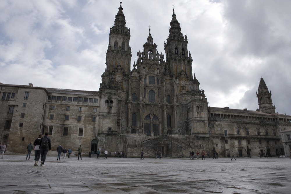 A baroque granite cathedral facade rising above a wide square with a flagstone pavement at dusk