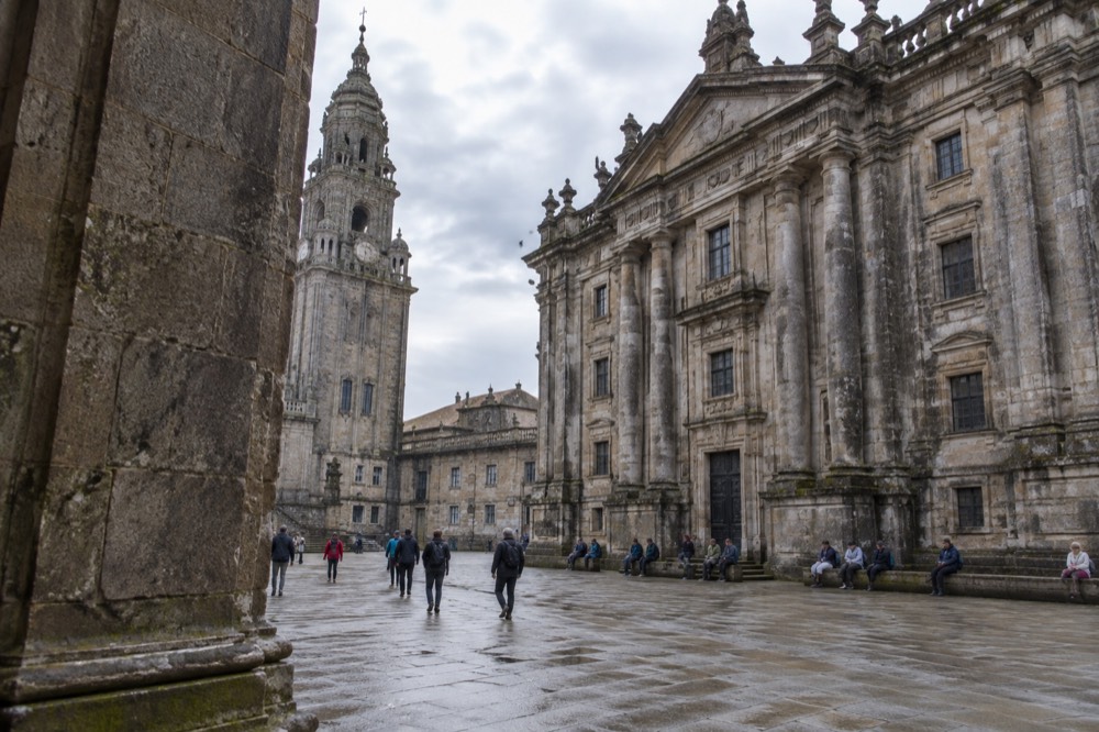 View across the square between Santiago de Compostela Cathedral and the San Martino Pinario monastery facade with pilgrims resting on benches