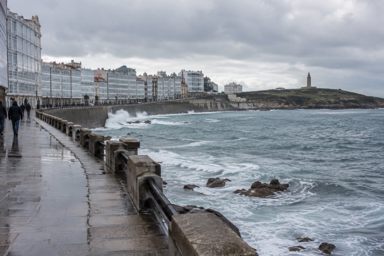 Oceanfront promenade of A Coruna with waves breaking against the sea wall and apartment buildings along the bay