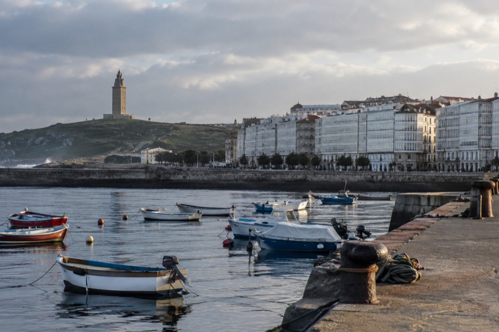 Tall stone lighthouse tower standing on a green headland above the Atlantic with the city behind it