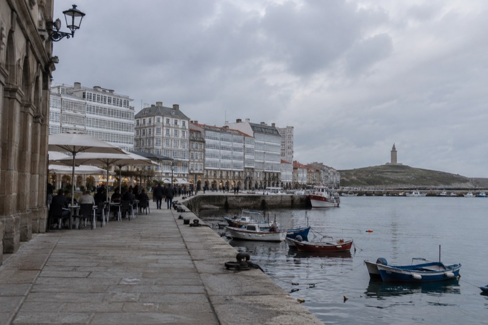 Old town square in A Coruna with arcaded stone buildings, café tables and pedestrians in the late afternoon