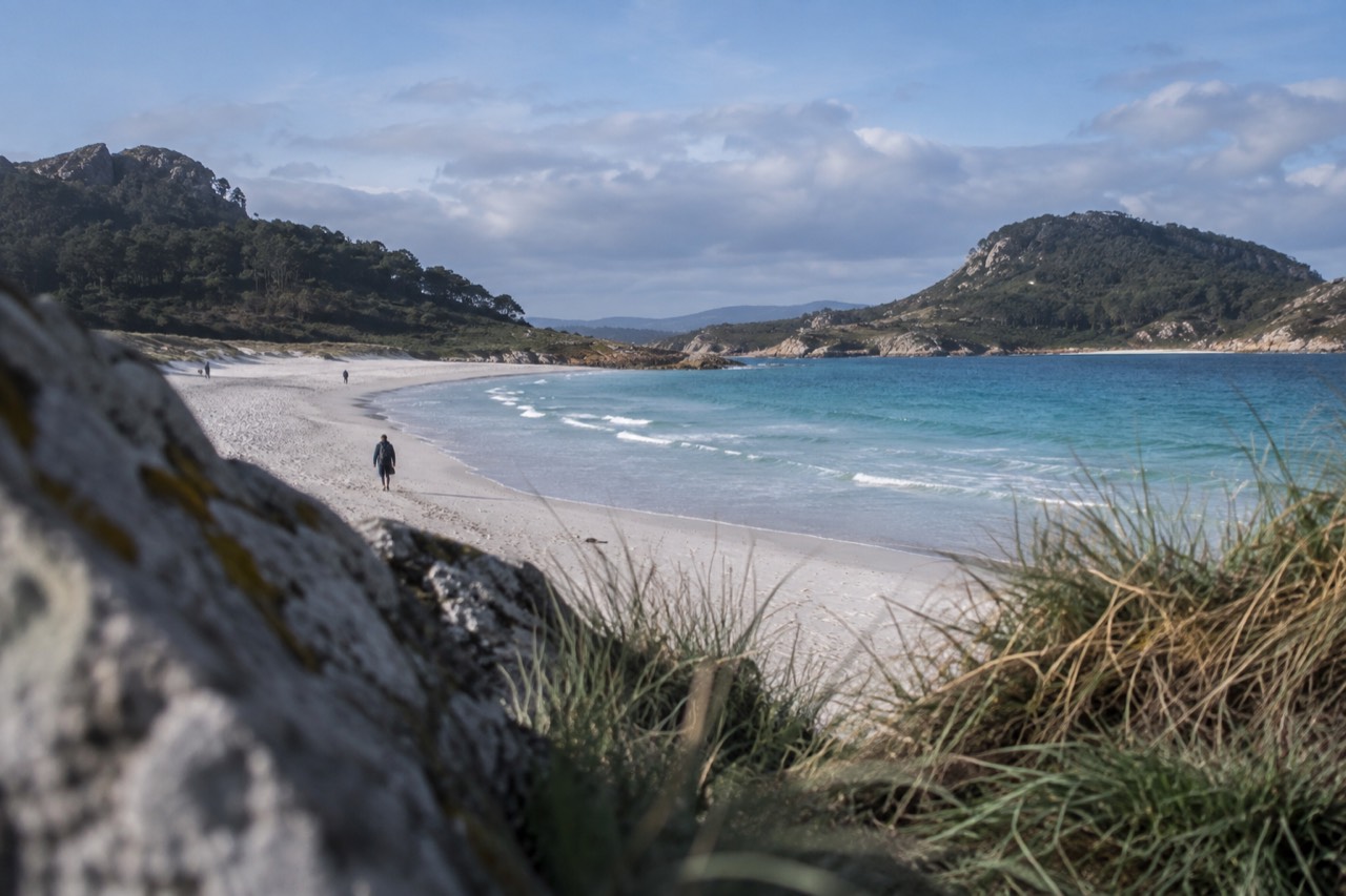 A sheltered white-sand beach curving between two green islands under a clear blue sky