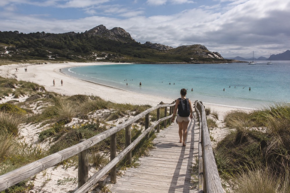 Turquoise shallow water over pale sand with people swimming near a wooden walkway