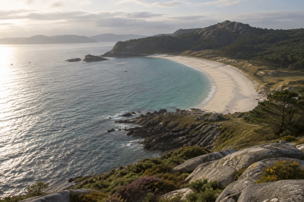 The long curve of a white beach seen from a high island path at golden hour
