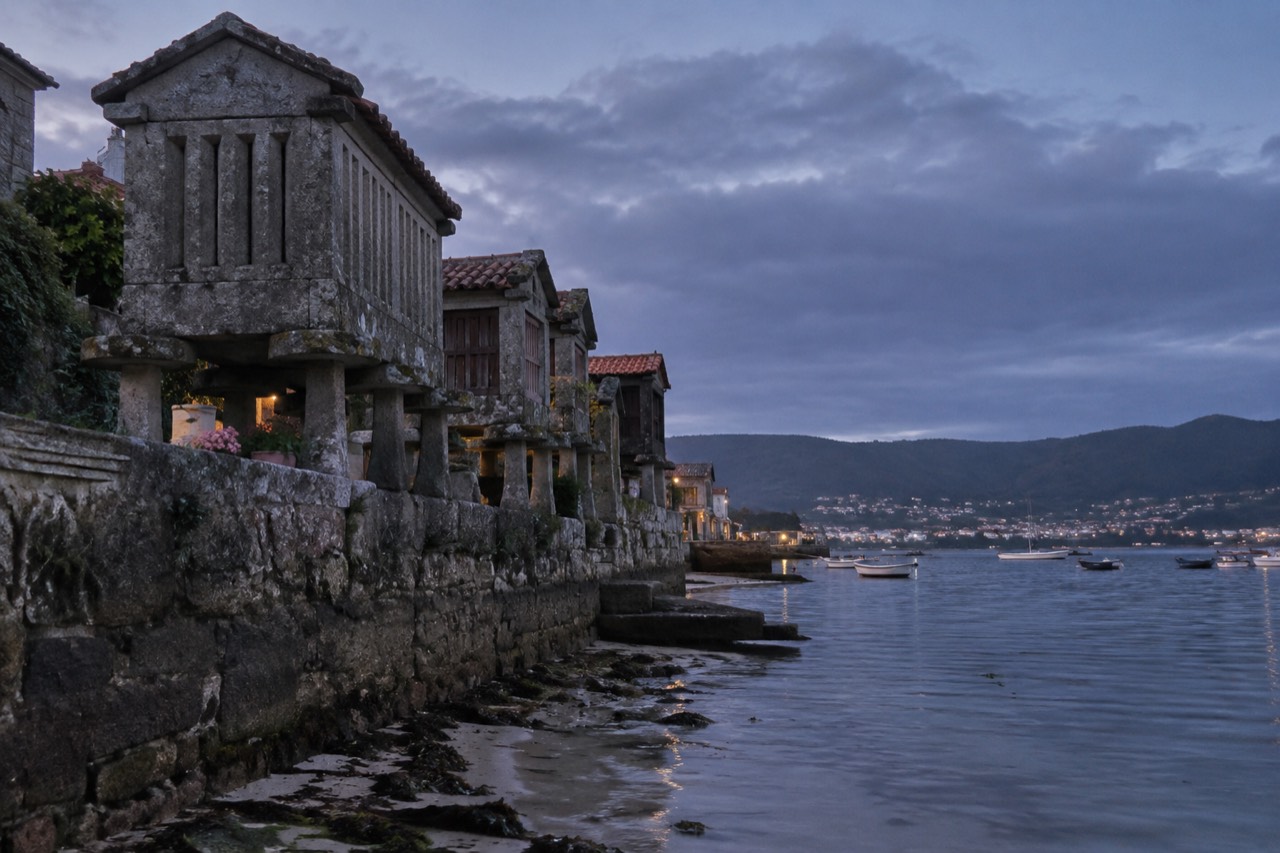 Stone hórreos standing on pilings at the waterline in Combarro, with the ria and small boats behind them