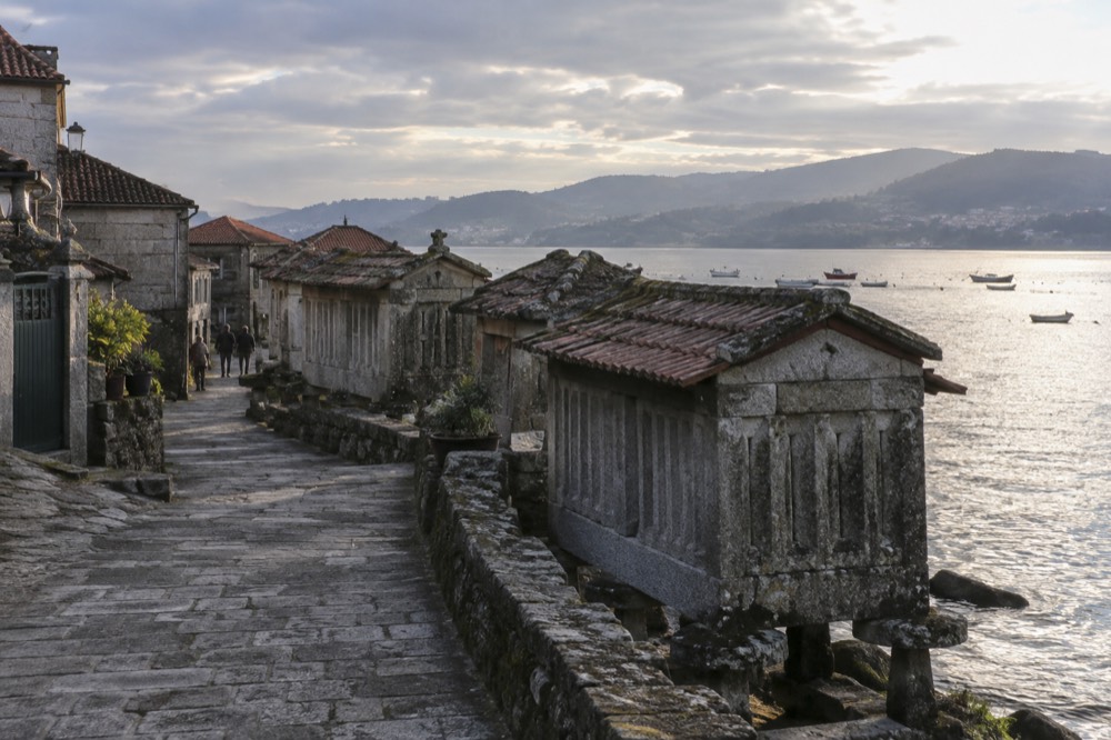 Late-afternoon light over the Combarro waterfront with hórreos in silhouette against the ria