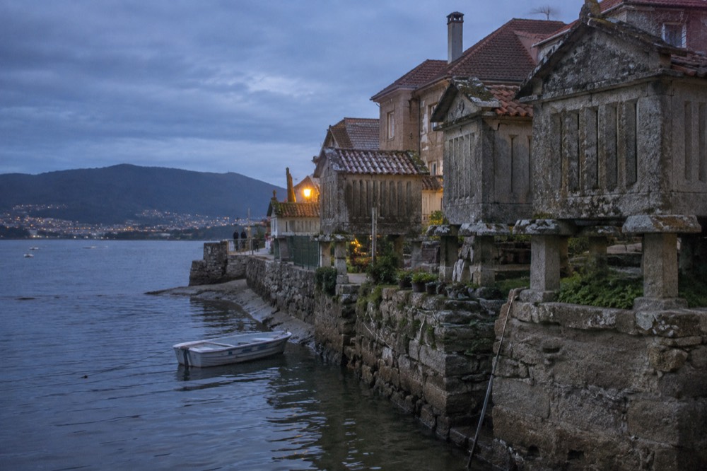 A small boat moored in shallow water beside the stone hórreos at Combarro's shoreline