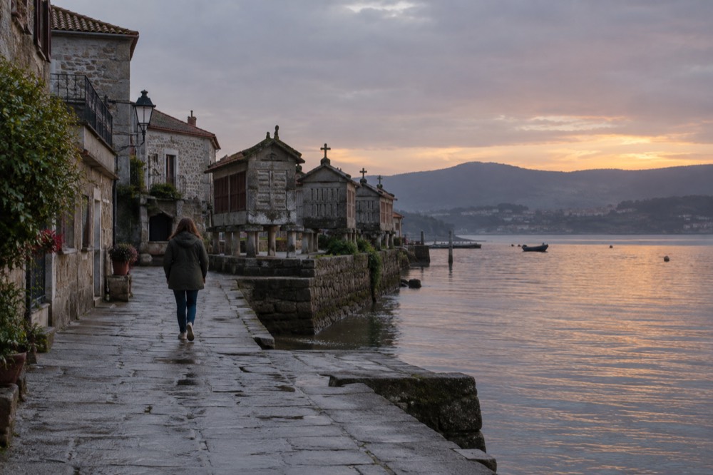 The calm water of the Ria de Pontevedra seen from the Combarro shoreline at dusk, with the silhouettes of hórreos along the edge