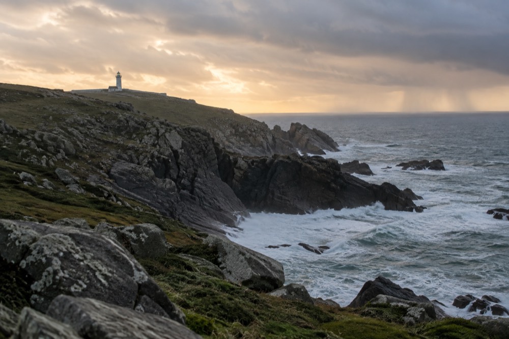 A stone lighthouse on a green headland above the Atlantic Ocean