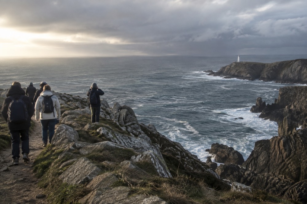 A tour group looking out from a cliff path toward the open Atlantic horizon