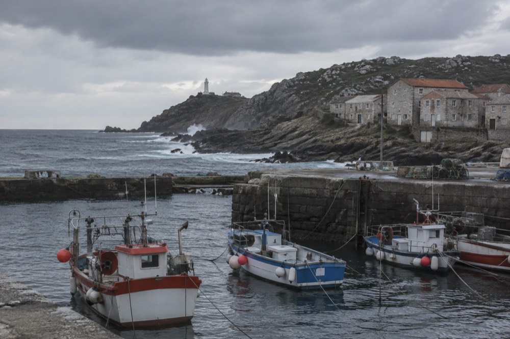 Fishing boats moored in a small Galician harbour with stone buildings behind