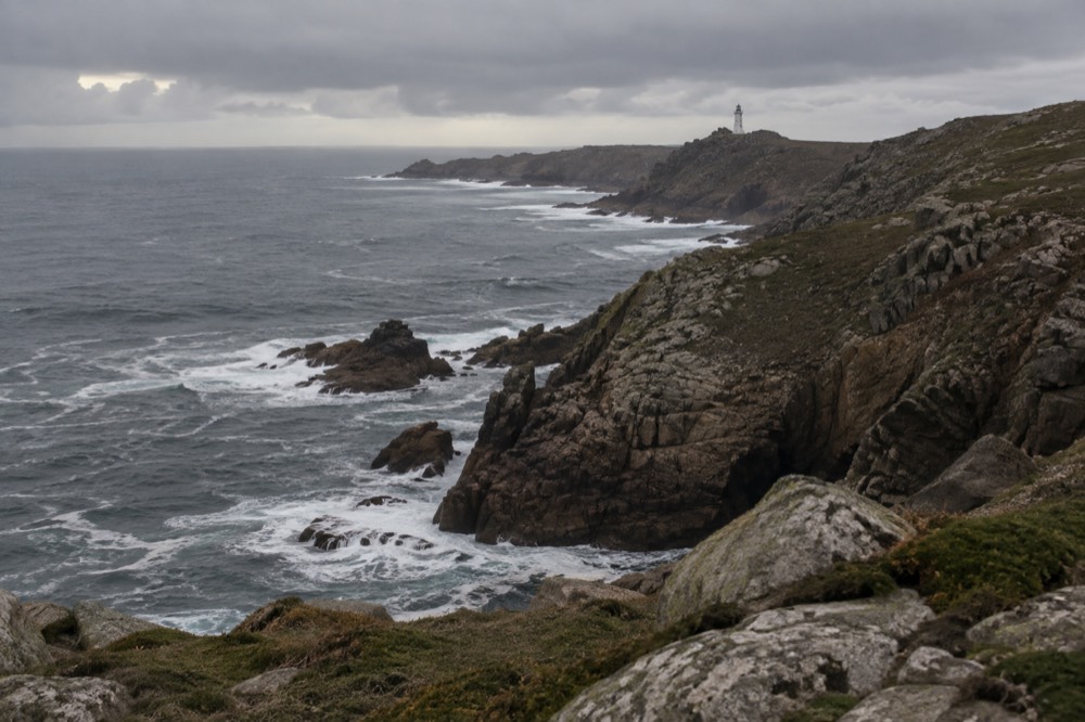 A rocky coastline curving toward a distant headland in soft evening light