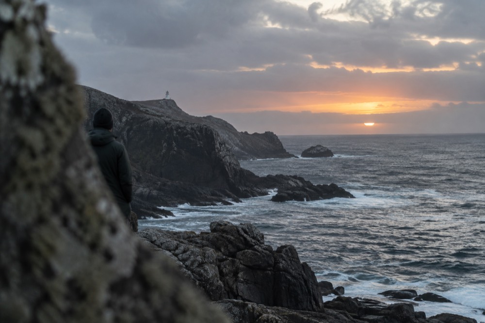 The sun setting into the open Atlantic beyond a dark rocky point of land